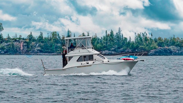 A white powerboat sailing in a lake near a rocky island.