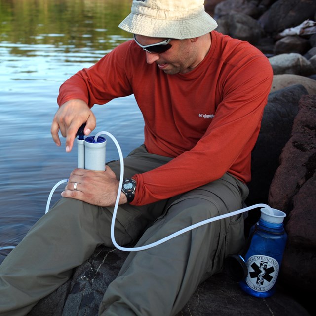 Person sits on lakeshore filtering water. 