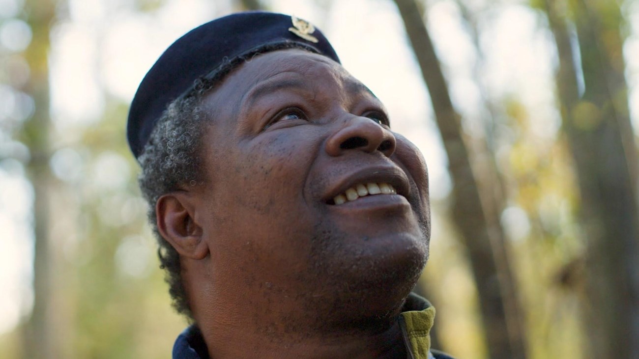 Man with short gray hair looks up towards the sky and smiles. Trees are behind him.