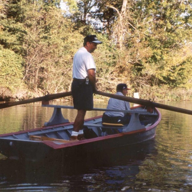 man standing on a small boat that's gliding down a bayou