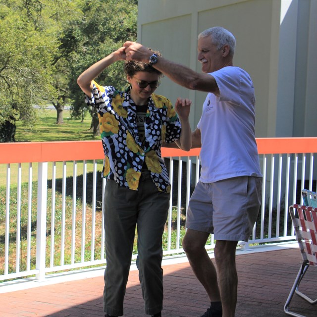 A man and woman hold hands and stand close together on a porch outside.