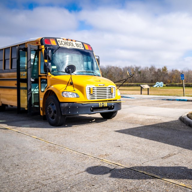 A school bus with a park ranger in a safety vest in front of it.