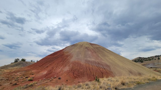 A red and tan hill with gray clouds above.