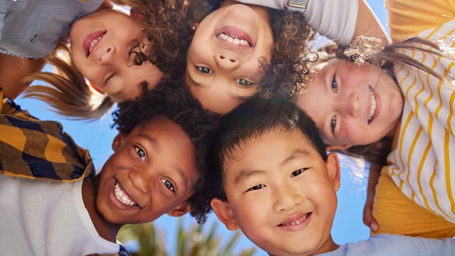 A group of young kids huddle and smile at the camera. 