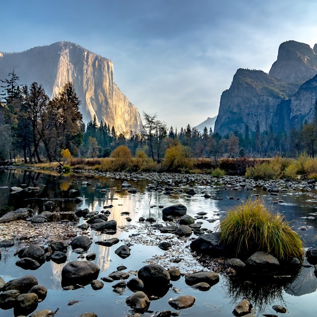 A scenic photo of water, rocks and trees against a mountain backdrop. 