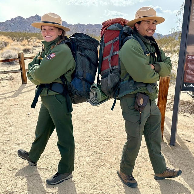 Two rangers wearing large backpacks and standing back to back to each other