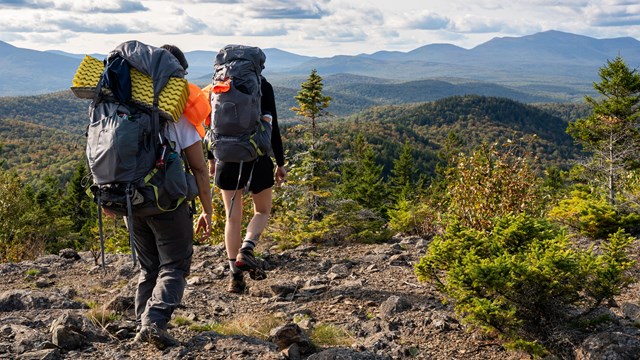Two backpackers on the summit of Lunksoos Mountain with other mountains in distance.