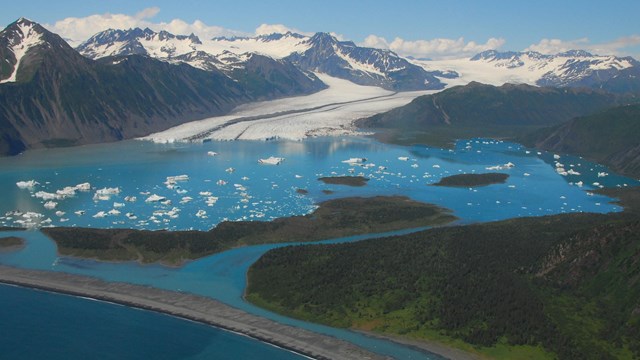 A lagoon with floating icebergs, surrounded by mountains and a glacier flowing into the lagoon.