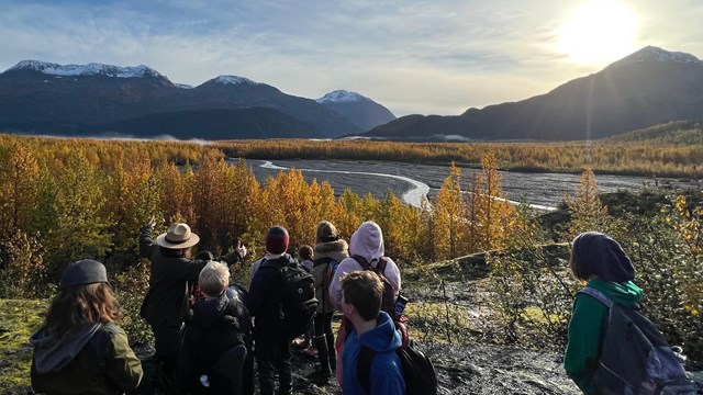 A ranger shows a valley of fall-colored trees to students