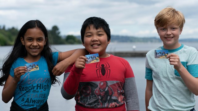 Three kids hold up their 4th Grade Pass