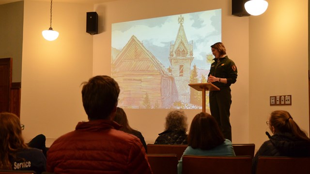 A ranger talks to people in front of a projected presentation