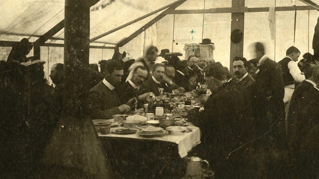 people sit at a long table inside a dining tent