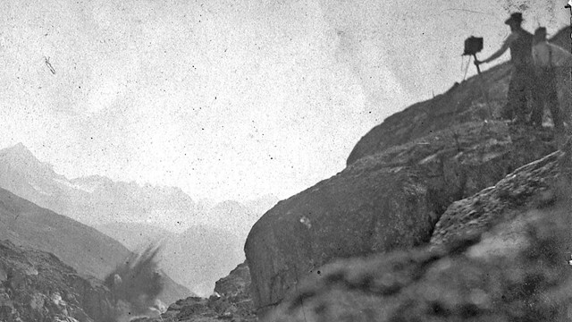 Black and white image of two people photographing a rocky blast