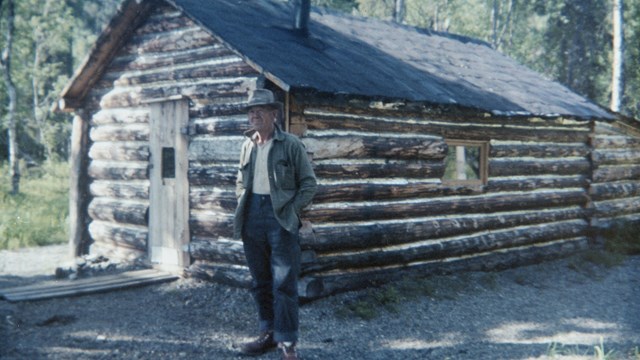 a man stands next to a wood cabin