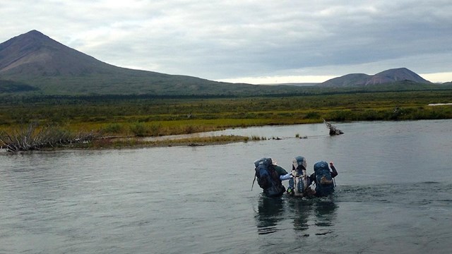 3 backpackers wade through a river