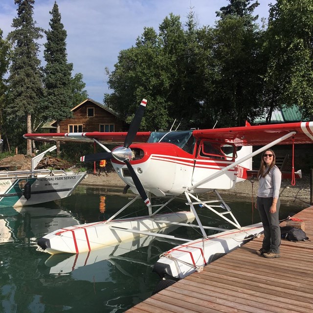 a woman stands on a dock next to a plane and a boat