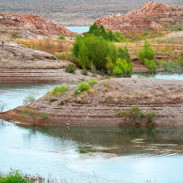 Winding water way through the desert with some green bushes. 