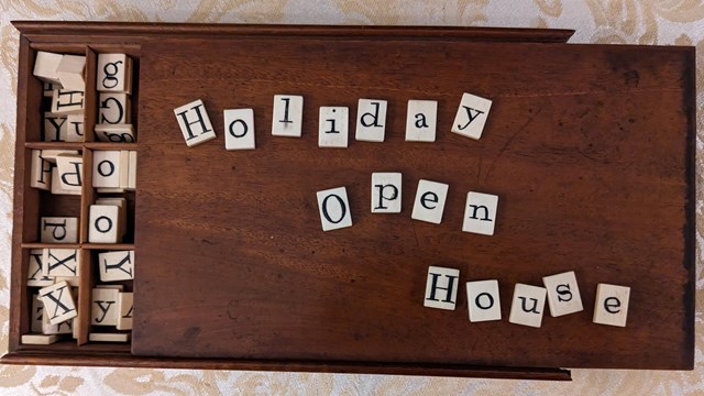 Tiles from a 19th century word game spell out Holiday Open House; on top of a wooden box