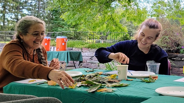 two people sit and paint at table outdoors