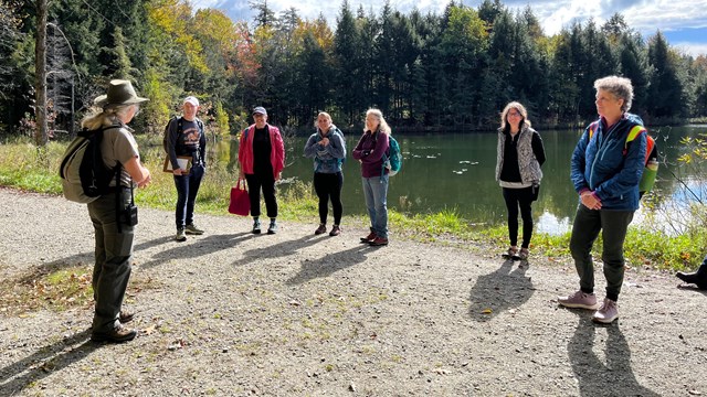 A group of visitors talk to a park ranger in front of a pond