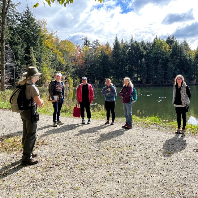 A group of visitors talk to a park ranger in front of a pond