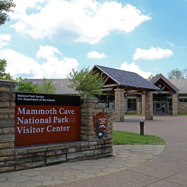 A stone building with a large brown sign in front. 