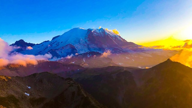 A glaciated mountain (Mount Rainier) sits under the vibrant colors of sunset.