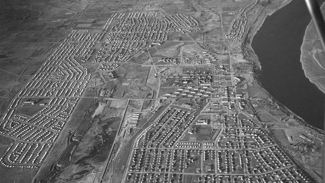 Aerial black and white photo of a city beside a river. 