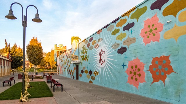 Downtown pedestrian block with benches, street lights, and colorful mural painted brick wall.