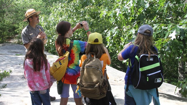 A ranger and several kids are on a path. 