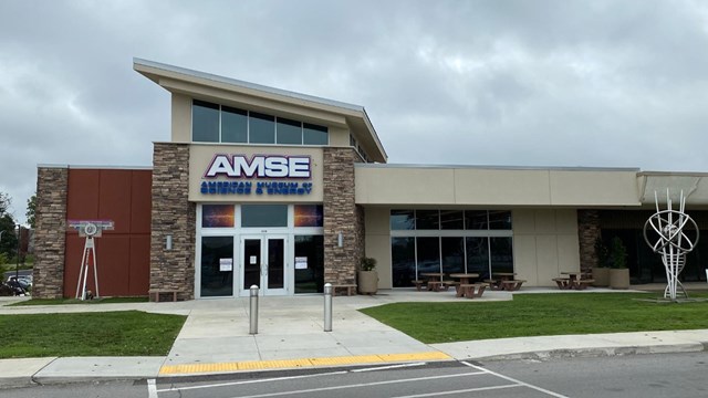 Exterior image of a museum in a strip mall with a sloped roof. The sign o