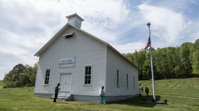  A white wooden church on a grassy hill with a flagpole to the right.