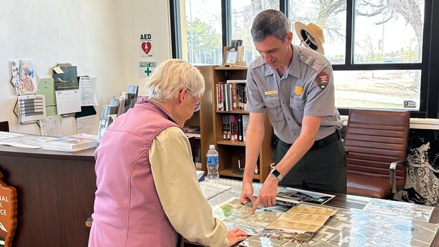 A park ranger points out something on a map to a visitor.