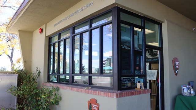 The exterior of a building with large windows and an NPS arrowhead sign on the wall.