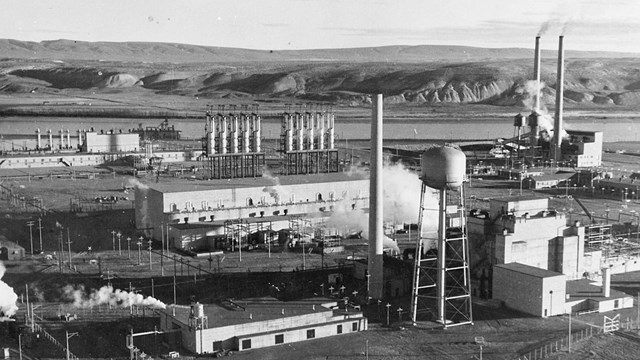 Black and white photo of an industrial complex along a river. 