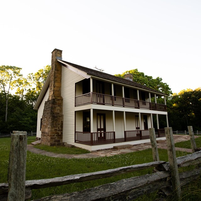  Two-story framed cream colored house chimney and porches with hand railings on both floors.