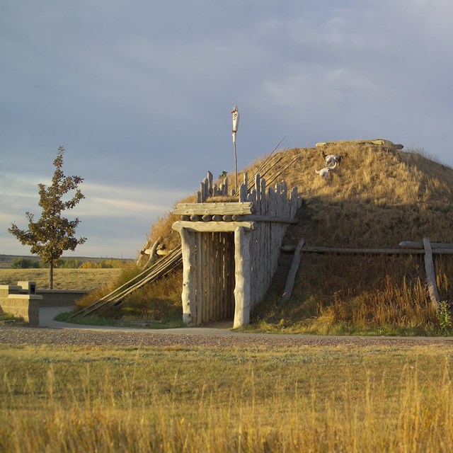 Earthen structure that has a mound shape covered in grass with a door frame. 