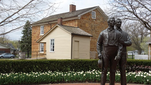 A metal statue of a person stands in front of a historic brick building.