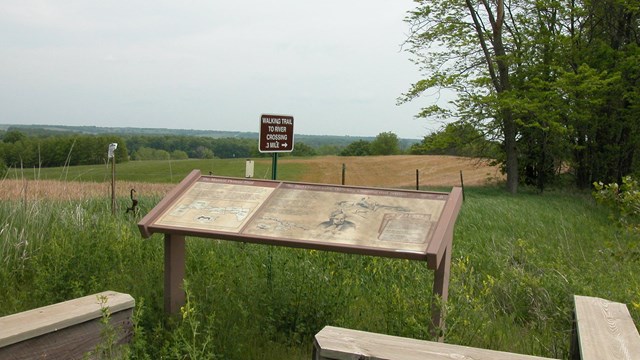 An exhibit sign sits in front of a grassy area in front of a muddy brown river.