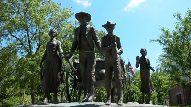 Bronze statue of pioneer people, pulling a two-wheeled, wooden hand cart.