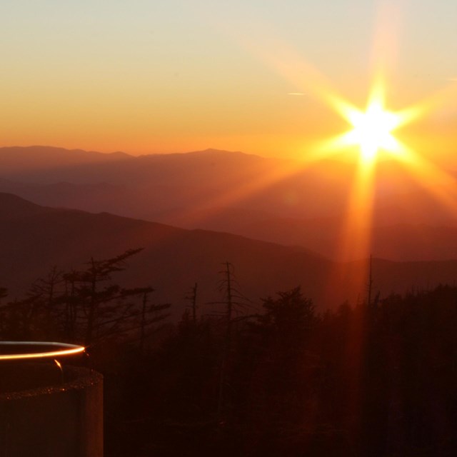 A yellow sun flares, making mountains into silhouettes.