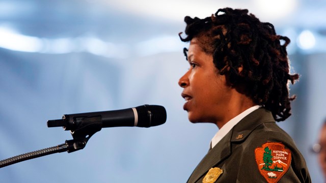 A park official talks from a podium with a National Park Service arrowhead on it