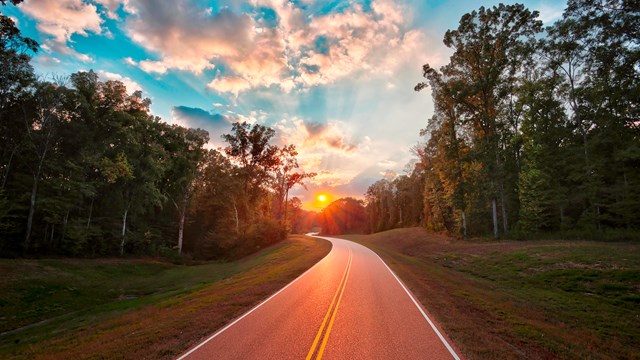 A two lane road heading into the sun rise.