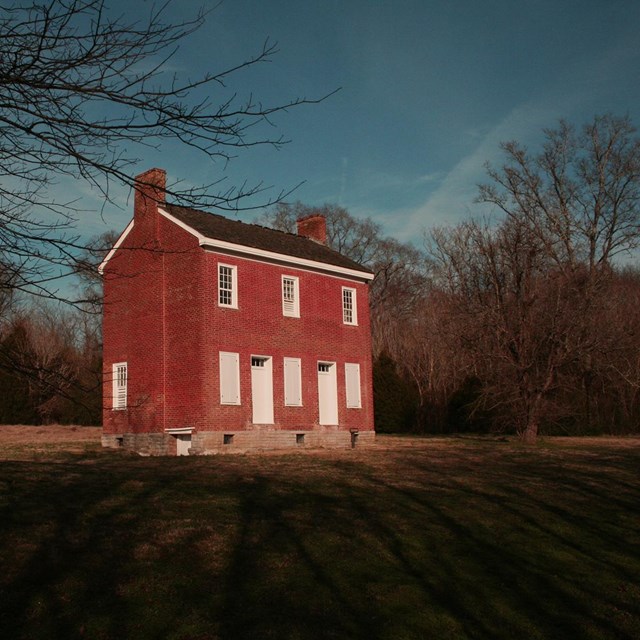 A two story brick house in a field surrounded by trees.