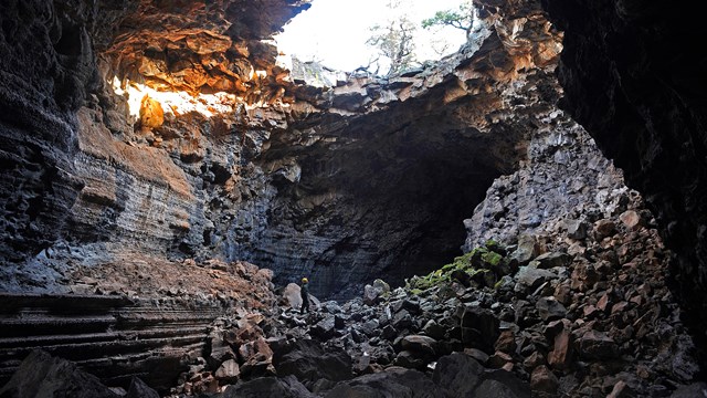 A man stands under a cave skylight