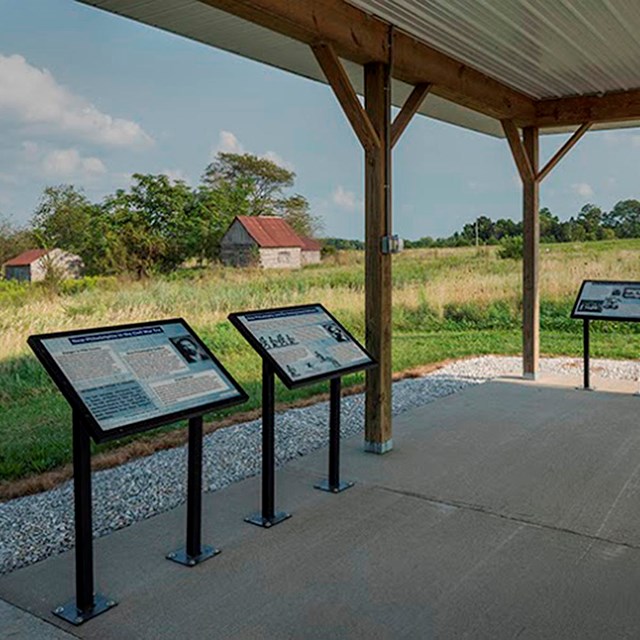  Four interpretive panels mounted under a covered, kiosk overlooking a prairie landscape.