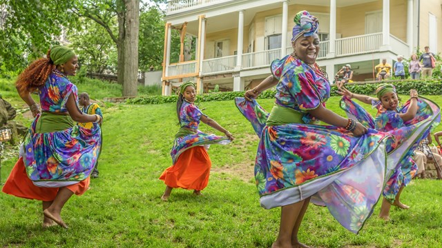 Women in traditional African dress dance on green grass