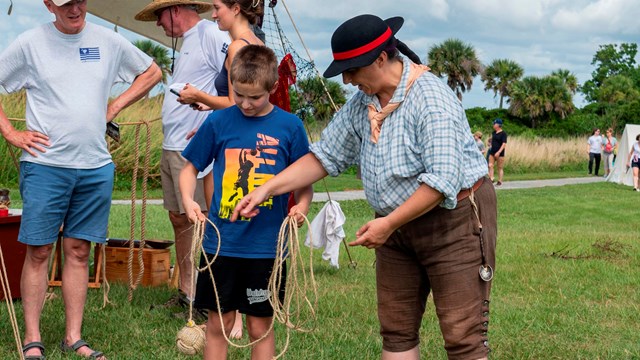 A person on historical costume shows a young person ball of rope on a rope at a special event.
