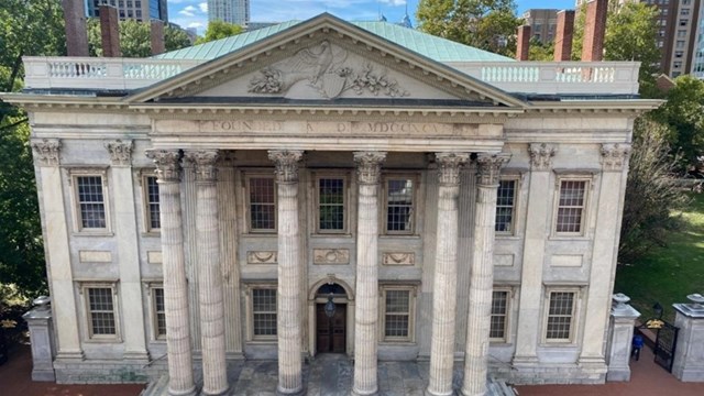 A stone building with large picture windows and columns at the entrance.