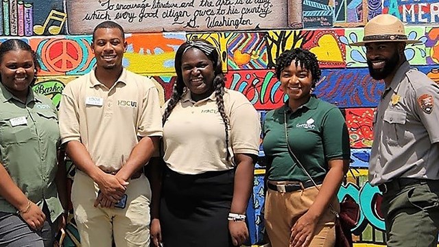 6 people pose for a photo in front of a colorful wall.